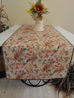 a vase with flowers on top of a table covered in a floral print cloth next to potted plants