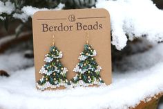 a pair of beaded christmas tree earrings sitting on top of a snow covered plant