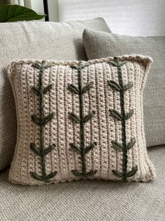 a crocheted pillow with green leaves on the front and back, sitting on a couch