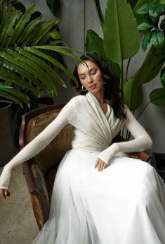 a woman in a white dress sitting on a chair next to some plants and greenery