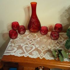 a red vase sitting on top of a wooden table next to glasses and plates,