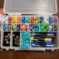 a plastic box filled with lots of different colored dices and pens on top of a wooden table