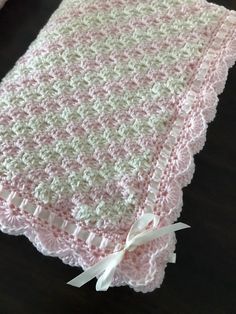 a pink and white crocheted blanket sitting on top of a wooden table next to a pillow