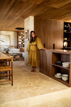 a woman in a yellow dress standing next to a wooden cabinet and counter with plates on it