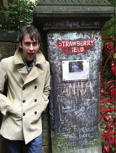 a man standing in front of a stone wall with writing on it and a sign that says strawberry field