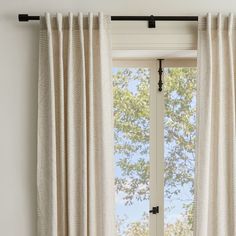 an open window with white curtains in front of it and a tree outside the window