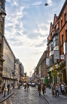 people are walking down an old cobblestone street in the city center at sunset