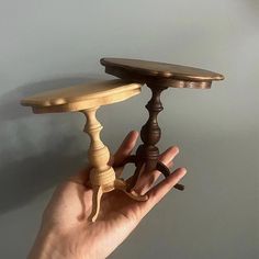 a hand holding a small wooden table with two smaller tables on it's sides