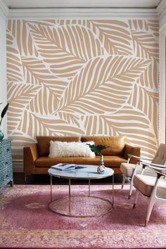 a living room with a couch, chair and coffee table in front of a palm leaf wallpaper