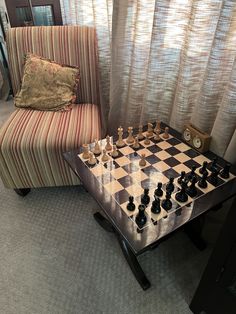 a chess board sitting on top of a metal table next to a chair and window