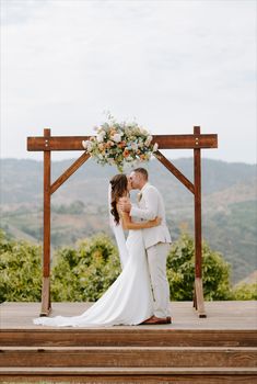 a bride and groom kissing in front of a wooden gazebo with flowers on it