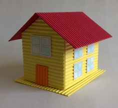 a small yellow house with a red roof on a white tableclothed surface, in the shape of a dollhouse