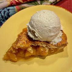 a piece of pie with ice cream on top sits on a yellow plate next to a flowered cloth