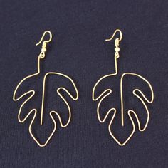 a pair of gold earrings with a large leaf on it's earwires