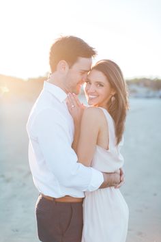 a man and woman standing next to each other on the beach with their arms around each other