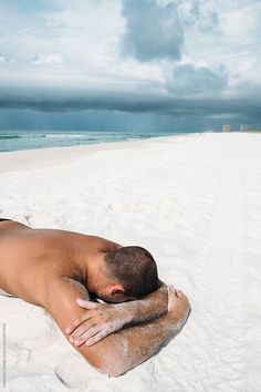 a naked man laying on the beach with his head in his hands and eyes closed