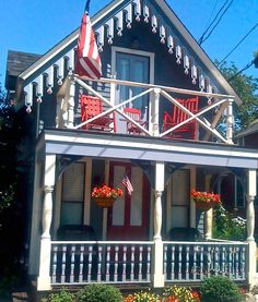 a red and white house with american flags on the porch, flowers in front of it