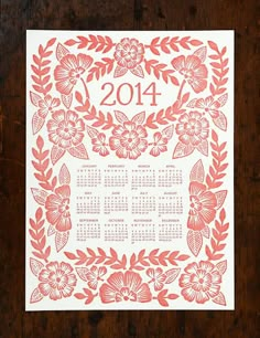 a red and white calendar on a wooden surface with flowers in the center, surrounded by leaves