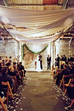 a couple getting married in front of an audience at a wedding ceremony with white draping