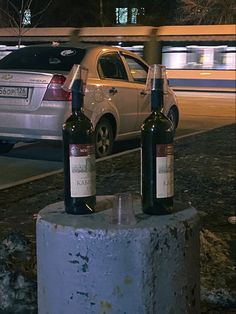 two bottles of wine sitting on top of a cement block next to a street with cars in the background