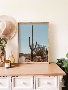 a desert scene with a cactus in the foreground and a hat on top of a dresser