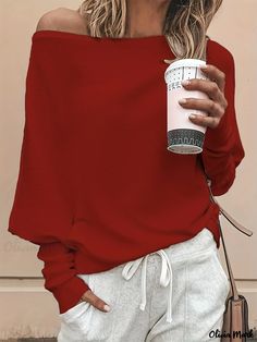 a woman wearing a red off the shoulder sweater and white pants holding a coffee cup