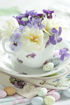 a tea cup filled with purple and white flowers on top of a saucer next to eggs