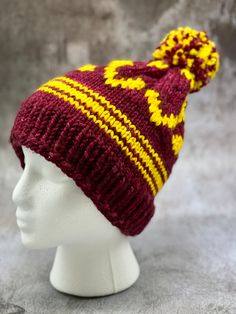 a white mannequin head wearing a maroon and yellow knitted beanie hat