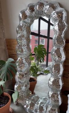 a mirror sitting on top of a table next to a potted plant in front of a window