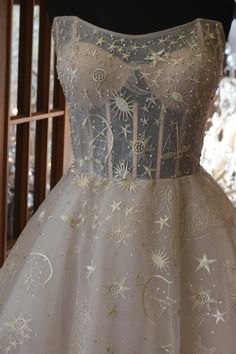 a white dress with gold stars and moon designs on the skirt is sitting on a mannequin