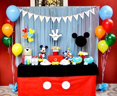 a mickey mouse birthday party with balloons, cake and desserts on a table in front of a red wall