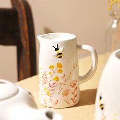 a white vase with yellow flowers and a bee painted on it sitting on a table