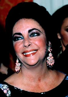 a woman with blue eyes and black dress smiling at the camera while wearing large earrings