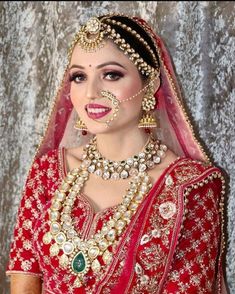 a woman in a red and gold bridal outfit with jewelry on her face, smiling