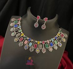 Traditional Indian-style jewelry, Silver oxidized choker necklace and Earring set is studded with an array of vibrant, multi-colored CZ Color stones, each encased in intricately designed Oxidized silver-tone frames that exude a vintage charm. The Color stones (green, red, blue, and black) are meticulously arranged in a symmetrical pattern, alternating between square and circular settings that draw the eye along the necklace's elegant span. Perfect for bridal wear, festive occasions, or as a stat Oxidized Choker, Symmetrical Pattern, German Silver Jewelry, Color Stones, Kundan Necklaces, Cz Jewelry, Necklace And Earring Set, Wedding Jewellery Necklace, German Silver