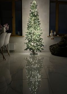 a white christmas tree is lit up in the middle of a living room with windows