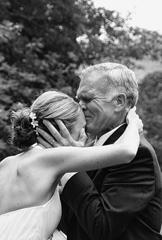 an older man and woman embracing each other in black and white, with trees in the background