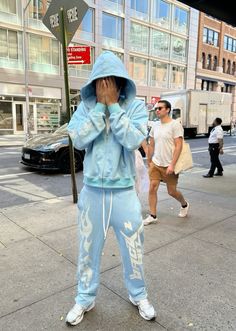 a person standing on the sidewalk covering their face with his hands and wearing blue sweatpants