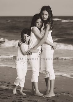 three girls standing on the beach with their arms around each other