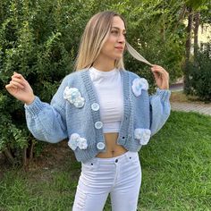 a woman wearing white jeans and a blue knitted cardigan with flowers on it