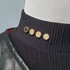 the back of a black leather jacket with three gold buttons on it's lapel