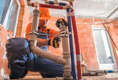 a man in an orange shirt working on pipes