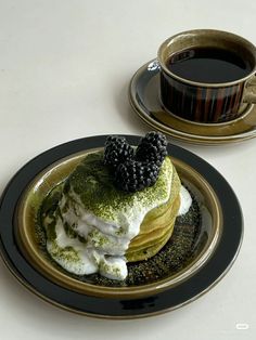 a plate topped with pancakes covered in whipped cream and blackberries next to a cup of coffee