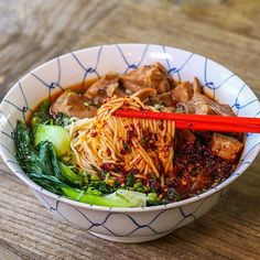 a bowl filled with noodles, meat and veggies next to chopsticks