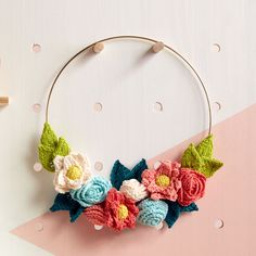 a crocheted wreath with flowers and leaves hanging on a pink, white, and blue background