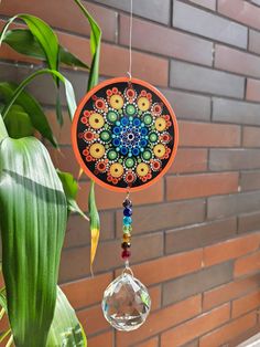 a colorful sun catcher hanging on a brick wall next to a plant with green leaves