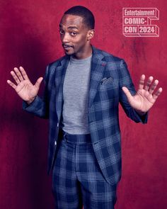 a man standing in front of a red wall wearing a suit and holding his hands out