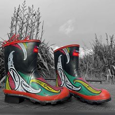 black and white photograph of rain boots with colorful design on the outstep, in front of corn stalks