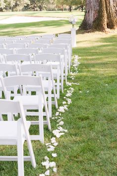 rows of white chairs lined up in the grass for a wedding ceremony with petals on the ground