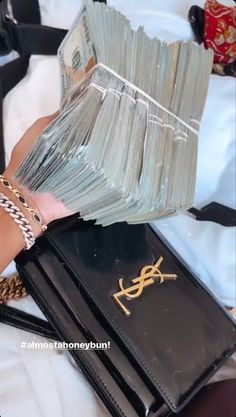 a woman's hand holding a stack of money in front of a purse with chains on it